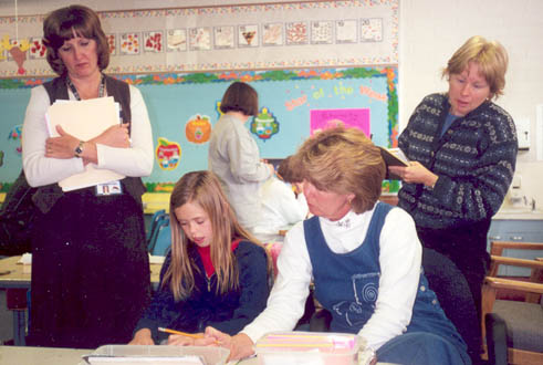 Three adults working with a student as she is reading